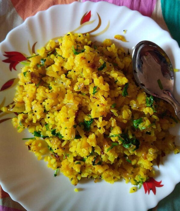 A plate of yellow rice garnished with herbs, placed on a white plate with a floral design.