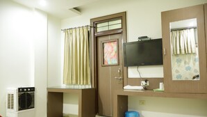 Una habitación de hotel con cama, escritorio, televisor, armario y cesto de basura.