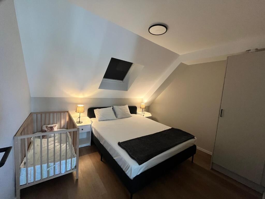 Een slaapkamer met een eenpersoonsbed, een ledikant, een nachtkastje, een lamp, een kast en een klein raam.