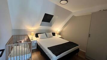 Een slaapkamer met een eenpersoonsbed, een ledikant, een nachtkastje, een lamp, een kast en een klein raam.