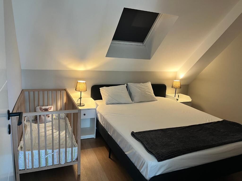 Ein Schlafzimmer mit Bett, Nachttischlampen, einem Babybett und einem Oberlicht.