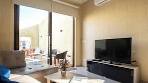A modern living room with a flat-screen TV, a sofa, a coffee table, and a balcony with chairs. - Narcisa - Luxury House w/ Pool, Cinema & Hot Tub (Ix-XagÄ§ra)