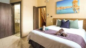 A hotel room with a bed, a painting of a coastal scene, and a view of a staircase. - Narcisa - Luxury House w/ Pool, Cinema & Hot Tub (Ix-XagÄ§ra)