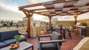 A rooftop patio with a pergola, outdoor seating, a grill, and a fruit basket. - Narcisa - Luxury House w/ Pool, Cinema & Hot Tub (Ix-XagÄ§ra)