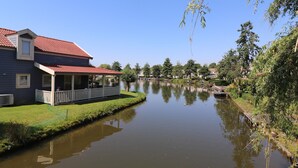 Ein Haus mit rotem Dach, einer Veranda und einem Teich davor.