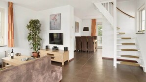 A modern living room with a sofa, TV, and a dining area with chairs and a table. - Bungalow in Zuytland by Water and Nature (Simonshaven)