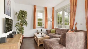 Een woonkamer met een bank, een bijzettafeltje, een houten kast, een potplant en een raam met gordijnen.