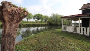 A treehouse with a white railing, a pond, and a building with a red roof. - Sun-Soaked Bungalow in Simonshaven (Simonshaven)
