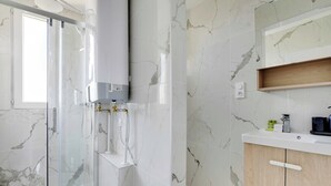 Un baño moderno con ducha acristalada, azulejos de mármol, calefacción integrada y un tocador de madera con espejo.
