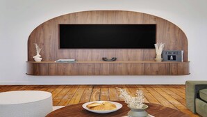 Un salon moderne avec un meuble TV en bois, un téléviseur à écran plat et une table basse ronde sur laquelle se trouve une assiette de croissants.