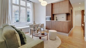 Un salon moderne comprenant un canapé, une table à manger, des chaises et un coin cuisine avec des meubles en bois et un four encastré.