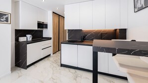 A modern kitchen with white cabinets, a black countertop, and a marble backsplash. - Large studio apartment with terrace and sea view (Cannes)