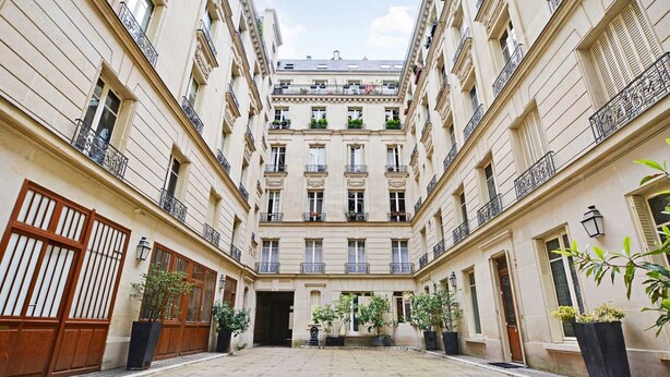 A courtyard with a central building featuring multiple balconies, large wooden doors, and potted plants. - Charming studio - 3P - Le Marais (Paris)