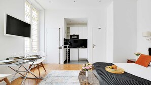 A modern, minimalist room with a dining area, a sofa, and a kitchen in the background. - Charming studio - 3P - Le Marais (Paris)