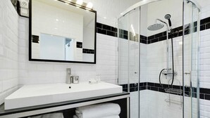 A modern bathroom with a white sink, black and white tiled walls, a glass shower enclosure, and a large mirror. - Charming studio - 3P - Le Marais (Paris)
