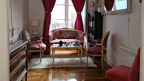 A room with a wooden floor, a sofa, a chair, a table, and a dresser. - Room in Apartment - Beautiful and Large Room in The City Centre (Valladolid)