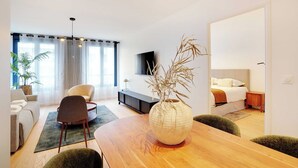 A modern living room with a sofa, armchairs, a wooden dining table, and a large vase with dried plants. - Sleek apartment in Levallois-Perret (Levallois-Perret)