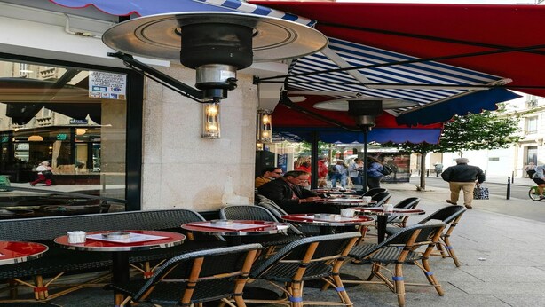 Outdoor seating with tables and chairs, a covered area with a striped awning, and a street view with pedestrians. - Sleek apartment in Levallois-Perret (Levallois-Perret)