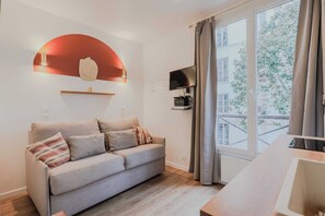 Un salon moderne avec un canapé, un téléviseur fixé au mur et une grande fenêtre agrémentée de rideaux.