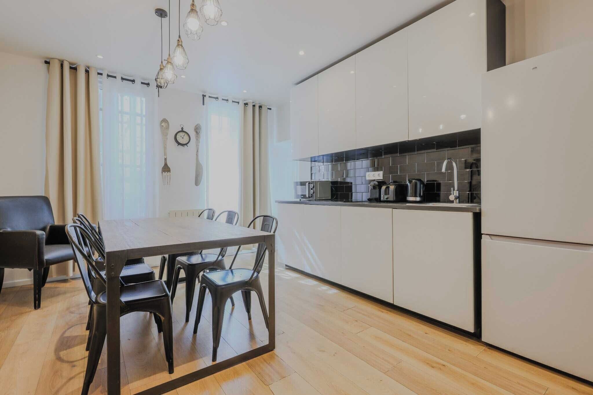 A modern kitchen with white cabinets, a black countertop, and a stainless steel range hood.