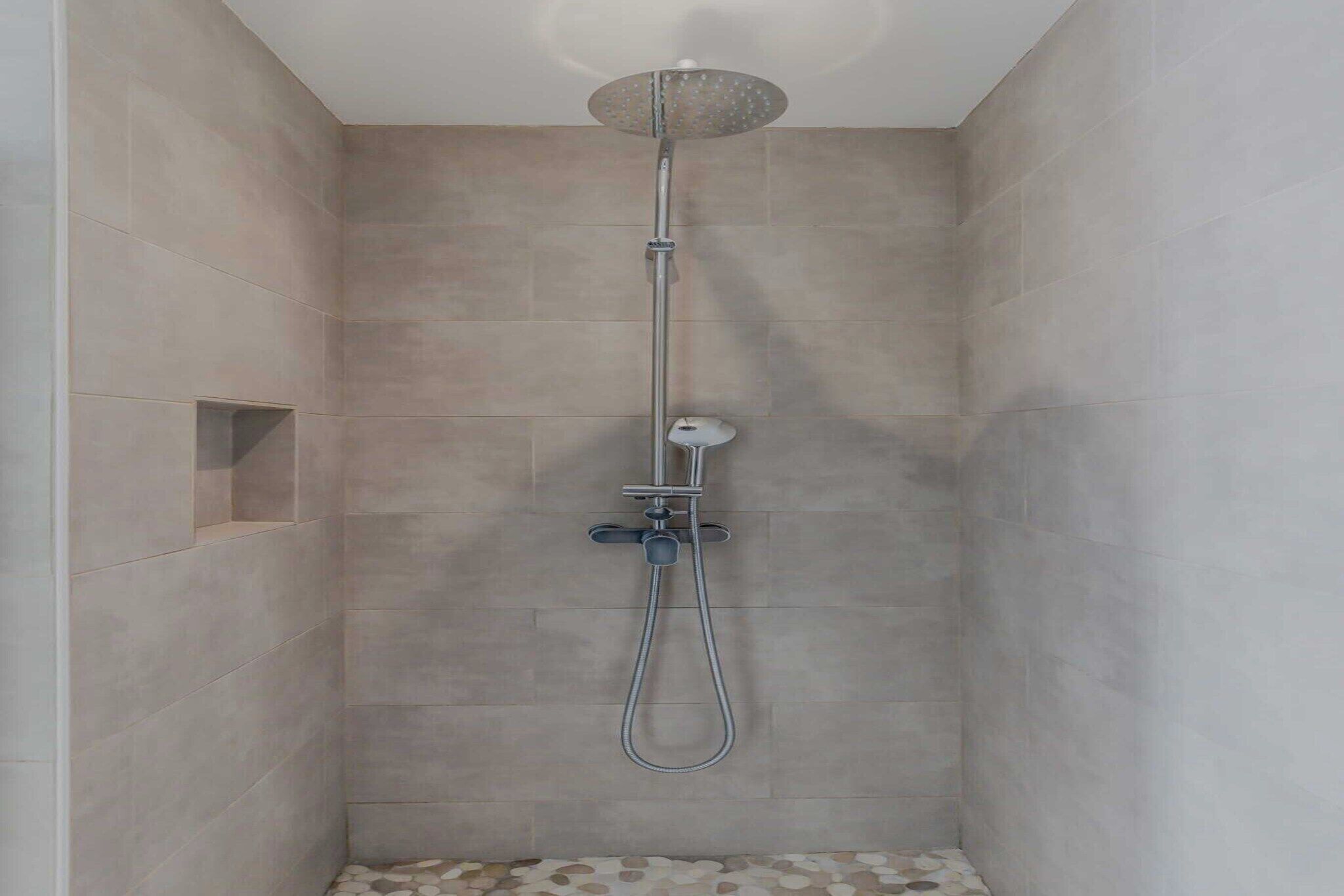 A shower with a handheld showerhead and a wall-mounted faucet.