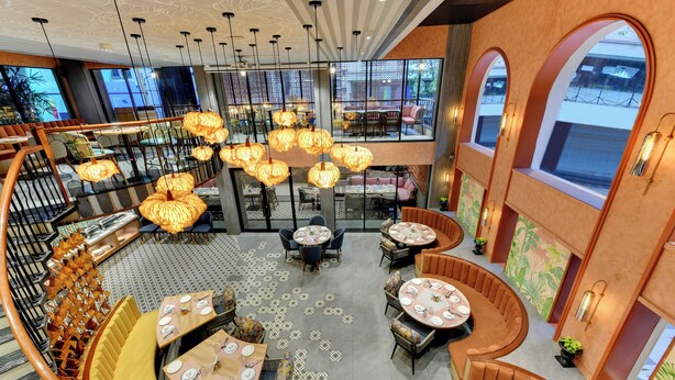 Un restaurante espacioso y moderno con varias zonas de comedor, incluyendo un espacio central abierto con mesas redondas y cabinas, y una zona de comedor separada con mesas y sillas altas.