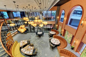 A spacious, modern restaurant with multiple dining areas, including a central open space with round tables and booths, and a separate dining area with high tables and chairs.