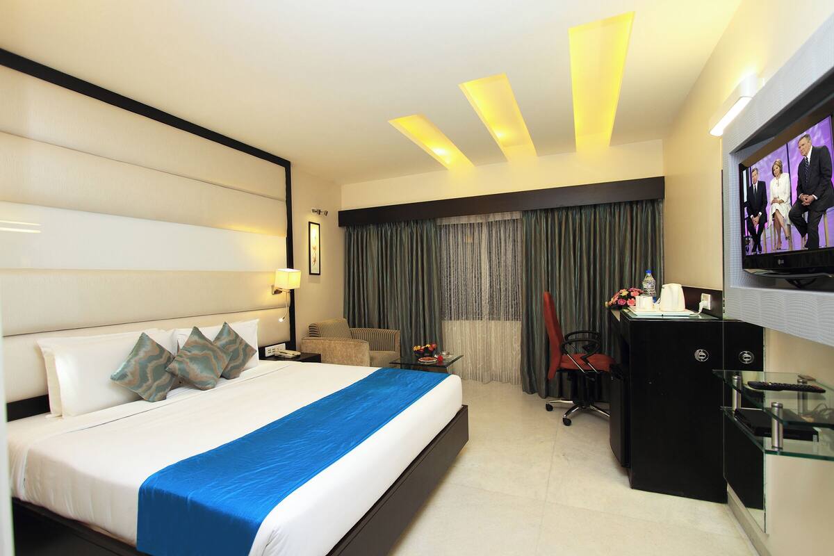 A hotel room with a large bed, a desk with a computer, a television, and a chair.