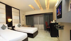 A hotel room with two beds, a desk, a TV, and a large window with curtains. - THE LUXANT HOTEL (Bengaluru)