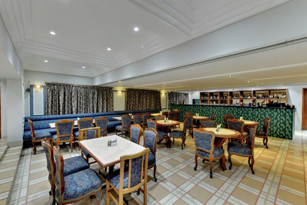 A restaurant with a checkered floor, blue upholstered booths, wooden tables, and chairs. - THE LUXANT HOTEL (Bengaluru)