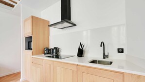 Une cuisine moderne avec un plan de travail blanc, des armoires en bois, une hotte noire, un évier en acier inoxydable et un bloc à couteaux noir.