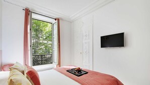 Une chambre avec un lit, une télévision, une fenêtre avec des rideaux et un balcon.