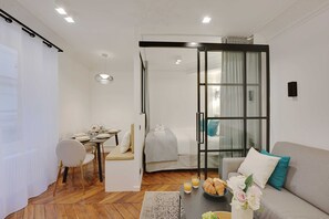 Una camera d'hotel moderna con zona pranzo, divano e porta vetrata che dà su un balcone.