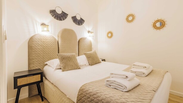 A neatly made bed with a textured headboard, a bedside table with a woven side panel, and decorative wall sconces.