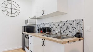 A modern kitchen with a microwave, coffee maker, and toaster on the counter, a clock on the wall, and a patterned backsplash.