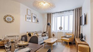 A modern living room with a dining area, a sofa, a TV, and a large window with curtains.