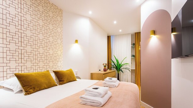 Una habitación de hotel moderna con una cama bien hecha, una mesita de noche con una planta y un espejo grande en la pared.