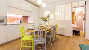 Una cocina moderna con armarios blancos, una mesa de comedor para cuatro personas y una silla de color amarillo brillante.