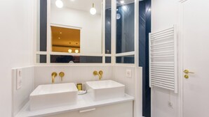 Un baño con dos lavamanos blancos, accesorios dorados y un espejo grande.