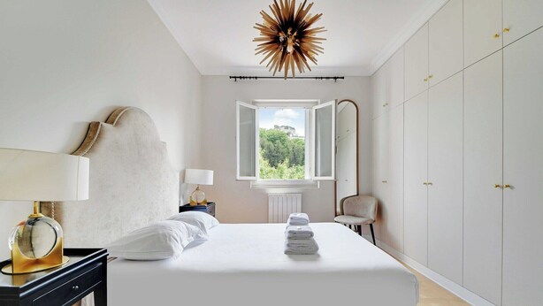 Un dormitorio con cama, lámparas de noche, una ventana con vistas, una lámpara de techo y un armario.