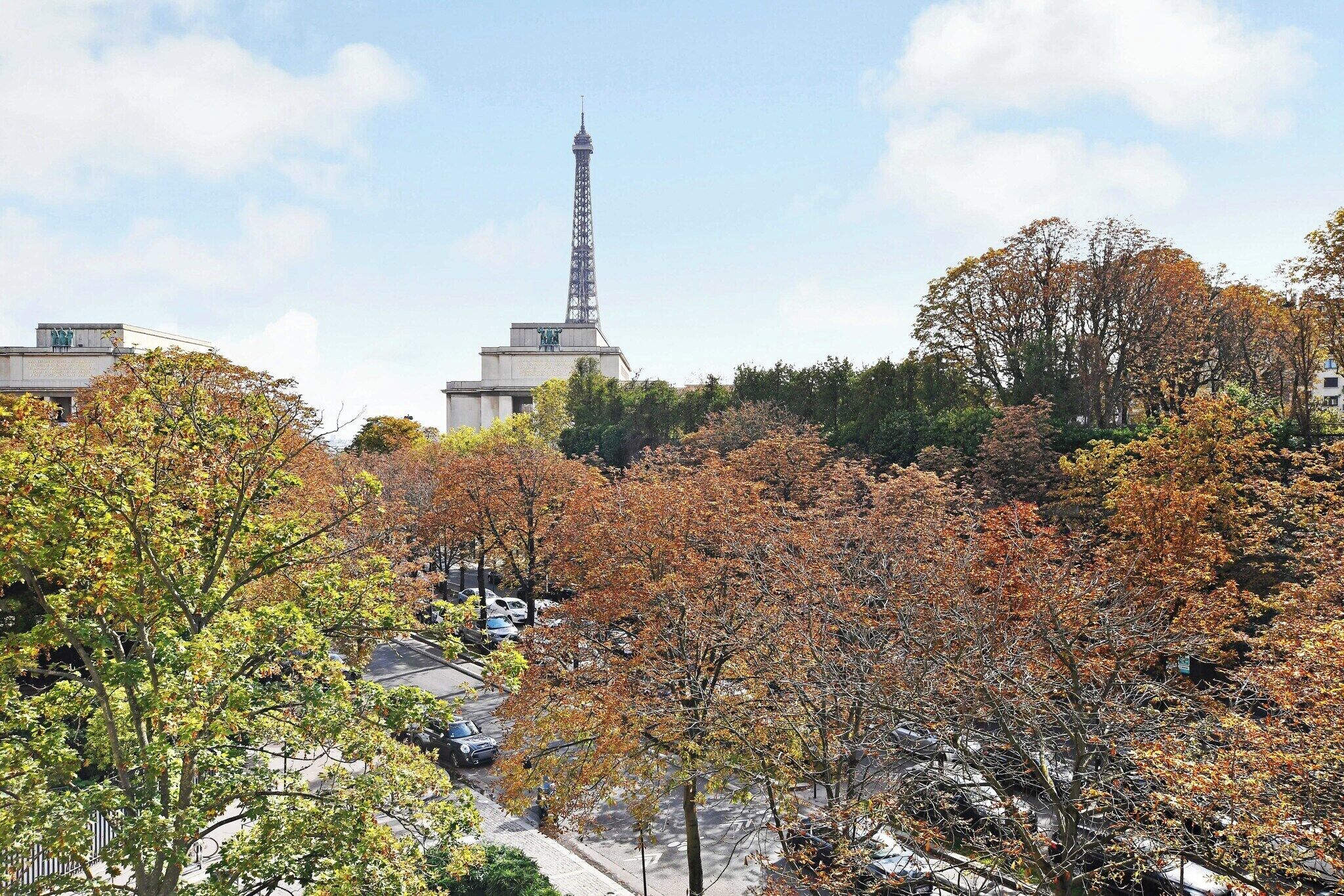 A view of the Eiffel Tower from a park with autumn trees.