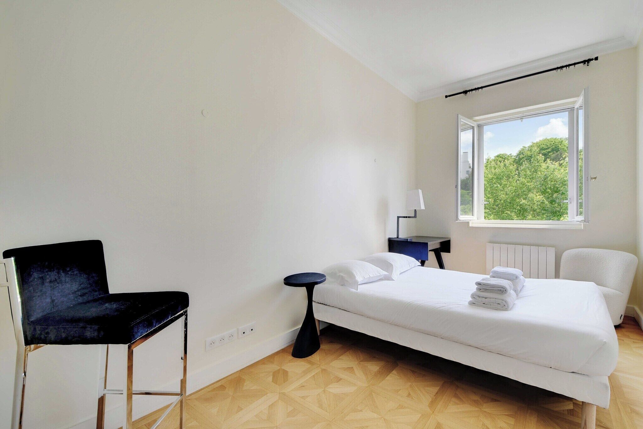 Habitación de hotel con cama, una silla, una mesita y ventana con vistas a zonas verdes.