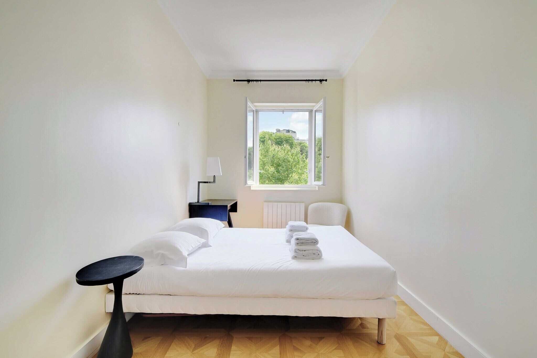 Une chambre à coucher avec un lit, une petite table, une chaise et une fenêtre donnant sur un paysage verdoyant.
