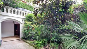 Un patio con un arco blanco, abundante vegetación y diversas plantas.