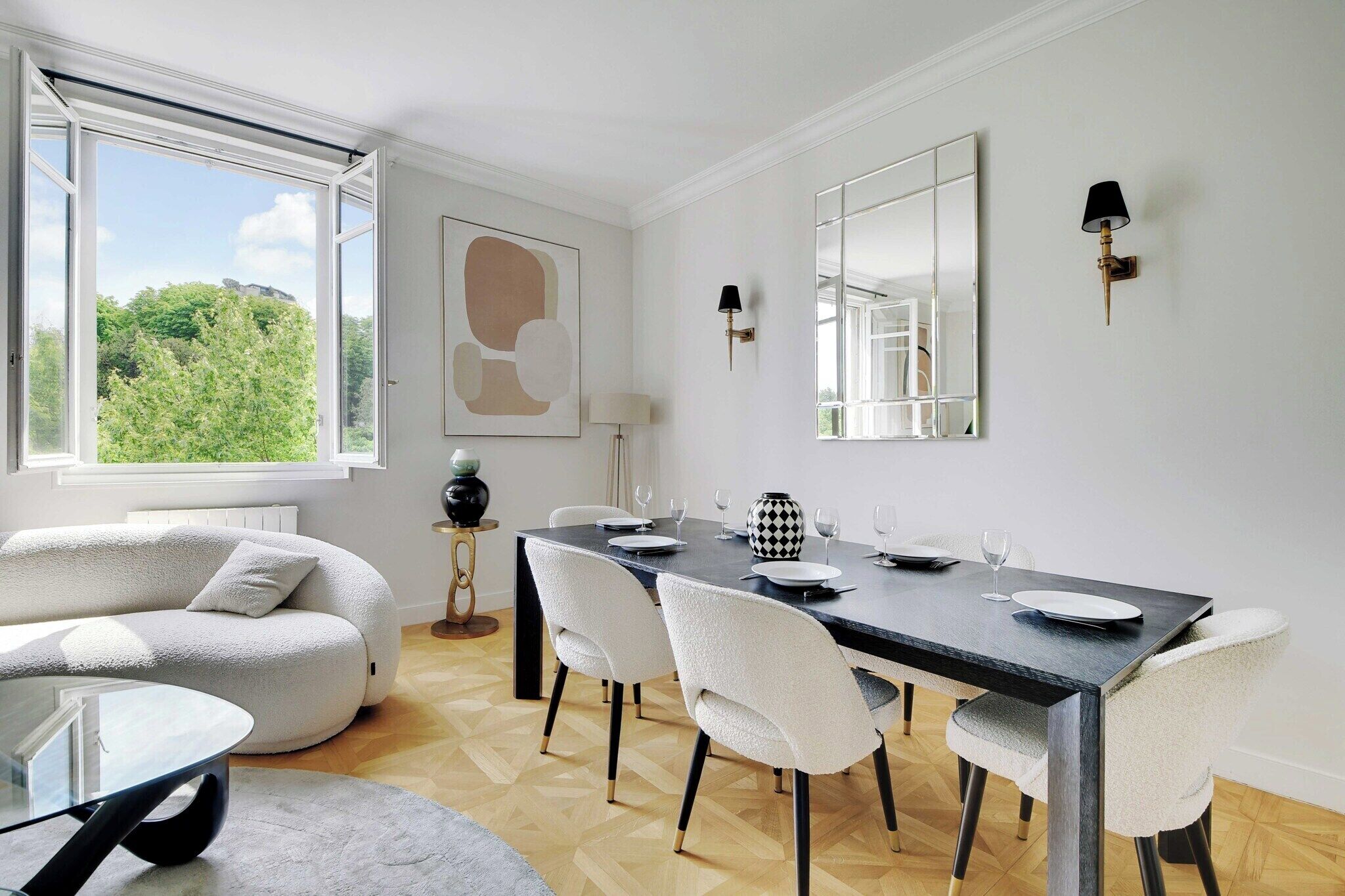 A dining area with a table set for four, a sofa, and a view of greenery outside.