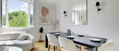 A dining area with a table set for four, a sofa, and a view of greenery outside.