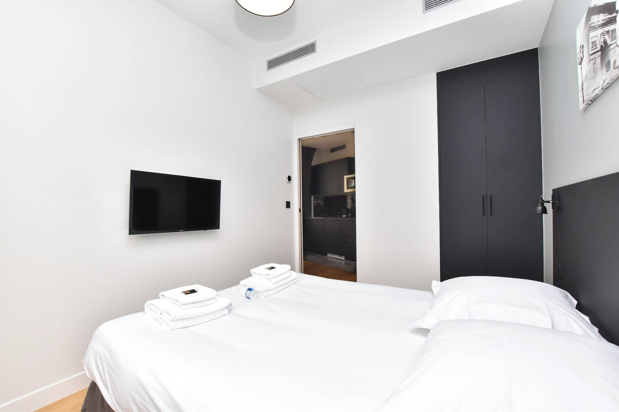 Quarto de hotel moderno com uma cama grande, televisão de tela plana na parede e um guarda-roupa escuro.