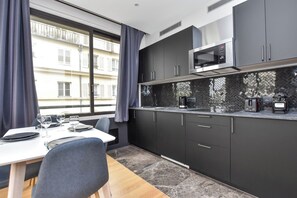 Una cocina moderna con armarios oscuros, microondas y cafetera. Cuenta con una mesa de comedor con sillas y una ventana con cortinas.