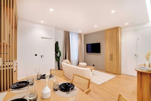 A modern living room with a dining area, a flat-screen TV mounted on the wall, and a large window with curtains. - Authentic apartment - 3BR/6P - Moulin Rouge (Paris)