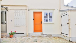 Ein Gebäude mit einem mit Fliesen ausgelegten Innenhof, einer leuchtend orangefarbenen Tür und einem weißen Fenster.